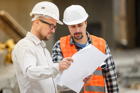 Male architect and developer discussing blueprints at construction site