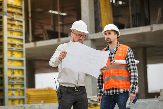 Male architect and developer discussing blueprints at construction site