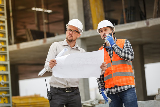 Male architect and developer with walkie talkie and blueprints at construction site