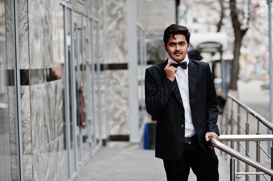 Young indian man on black suit and bow tie posed outdoor.