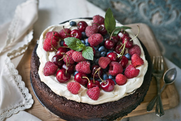 Chocolate cake with mascarpone on rustic background with raspberries, cherries, blueberries and mint leaves.