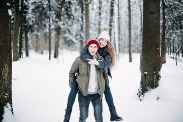 Fototapeta premium happy couple in love are walking in the snowy winter forest. Positive beautiful lovers in clothes for the cold time.