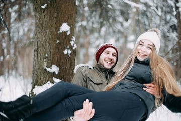  young couple in love are walking in the snowy winter forest. Positive beautiful lovers in clothes for the cold time.