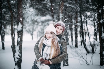 Obraz premium young couple in love are walking in the snowy winter forest. Positive beautiful lovers in clothes for the cold time.