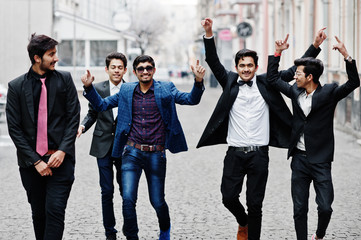 Group of 5 indian students in suits posed outdoor, having fun and dancing.