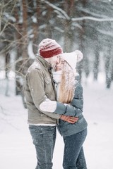  young couple in love are walking in the snowy winter forest. Positive beautiful lovers in clothes for the cold time.