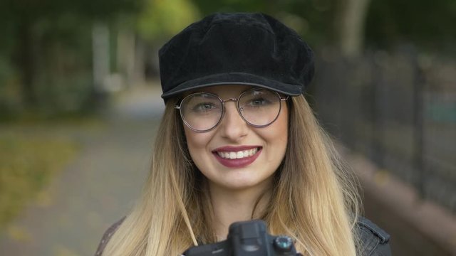 Professional young blonde woman photographer with digital camera taking pictures at city city park. Close Up, shallow depth of field, fall blurred background.