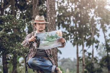 hiker man sitting and look at map and checking in the forest on stump.