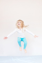 Fototapeta na wymiar Happy kid jumping over bed. Cute little blond girl having fun indoors. Happy and careless childhood concept