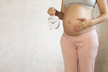 Pregnant women with the cute tummy holding alarm clock