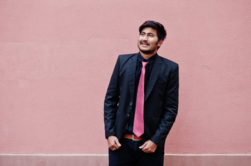 Young indian man on suit and tie posed against pink wall.