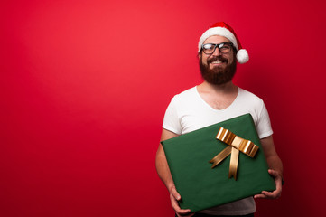 Happy bearded hipster man holding a big gift box over red background