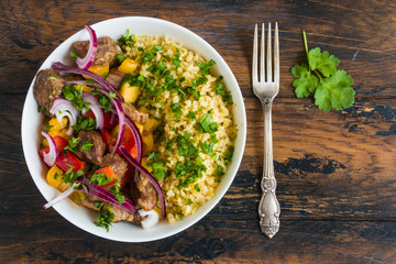 Big white bowl with beef cooked with vegetables, bulgur, red onion and fresh parsley, close-up, overhead