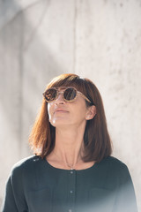 Street style Fashion portrait pretty middle age woman in stylish dark overall garment, smiling, sun glasses with wooden frame. Sunny day, city lifestyle
