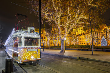 Festively decorated light tram (Fenyvillamos) on the move with Parliament of Hungary at Kossuth square by night. Christmas season in Budapest