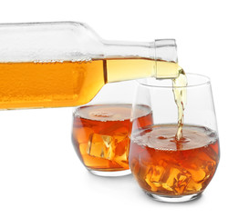 Pouring of whisky from bottle into glass on white background