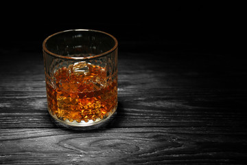 Glass of whisky with ice on wooden table against black background