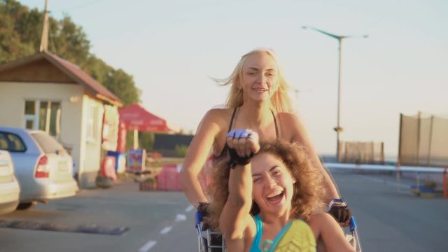 two cheerful girlfriends having fun on the street. women run with a cart from the supermarket and laugh. Soft light 4k
