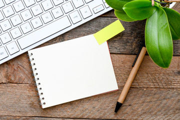 A blank notebook on the wood in the presence of a keyboard and a flower. View from above. High resolution photography.