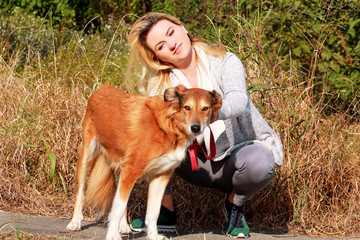 Pretty girl with his Shetland sheepdog dog at nature park outdoor is standing and posing in front of camera. Portrait of owner and Rough collie dog enjoys, resting and petting together on city street.