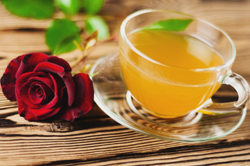 Glass cup with green tea and red rose on sprig on old wooden table. Saint Valentine's Day concept