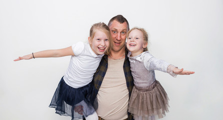 Fototapeta premium Happy loving family. Father and his daughters child girls playing together. The father is standing and holds girls. Kids stretching arms sideways. Father's day concept.