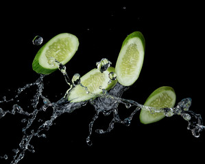 Fototapeta na wymiar Sliced cucumber with water splash or explosion flying in the air isolated on black background