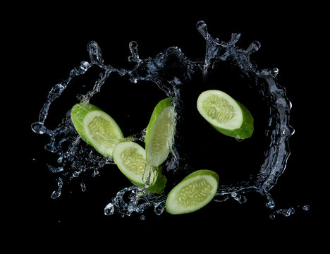 Sliced cucumber with water splash or explosion flying in the air isolated on black background