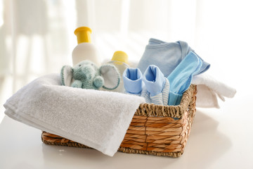Basket with baby clothes, cosmetics and toy on table