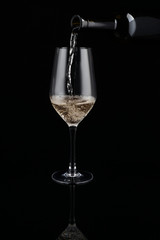 Pouring of white wine from bottle into glass on dark background