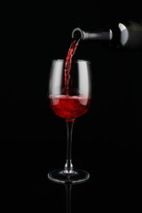 Pouring of red wine from bottle into glass on dark background