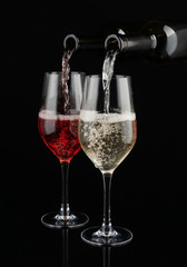 Pouring of white and red wine from bottles into glasses on dark background
