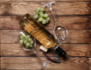 Bottle of white wine with glasses and corkscrew on wooden table