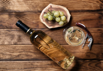 Bottle and glass of white wine on wooden background