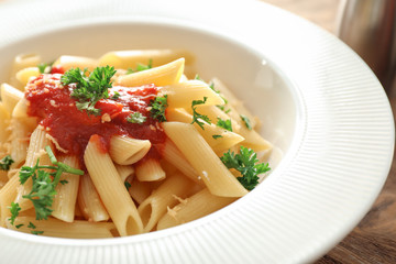 Plate with tasty penne pasta and tomato sauce on table, closeup