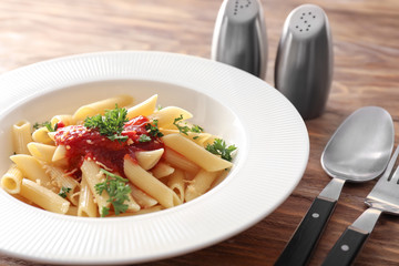 Plate with tasty penne pasta and tomato sauce on wooden table