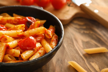 Frying pan with tasty penne pasta on wooden table