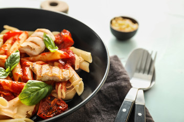 Plate with tasty penne pasta and tomato sauce on light table