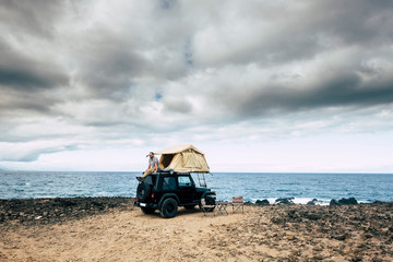 Adventure concept for caucasian man sit down and rest on the roof of his car with tent - traveler wanderlust lifestyle and different choice to live your life - feel the nature outdoor and enjoy