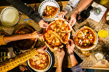 People eat pizza at festive table served for party. Friends celebrate with catering food on wooden table top view. Woman and man's yands take the pieces of italian pizza.