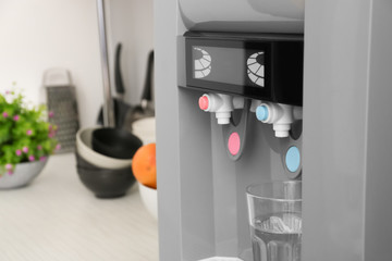 Modern water cooler with glass on kitchen table, closeup