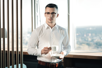 Dark-haired businessman having coffee break standing near the window