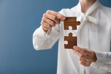 Woman with pieces of wooden puzzle on color background