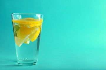 Glass of water with lemon on color background
