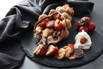Delicious bubble waffle with ice cream and fruits on slate plate