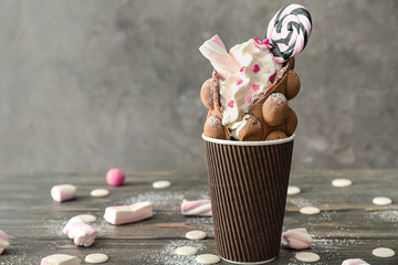 Delicious bubble waffle in cup on wooden table