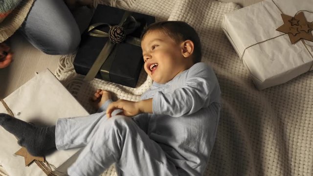 Little boy is tickled while he lies on the floor under the Christmas tree in slow motion