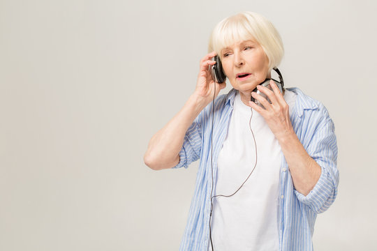 Wow, perfect music! Photo of mature woman 60s with gray hair slistening to music via headphones isolated over white background.