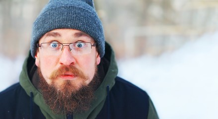 Young bearded guy with glasses and warm winter clothes in shock