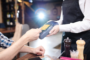 Close-up of unrecognizable man using cashless payment and putting wireless card to terminal in cafe